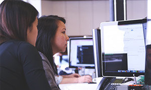 Two women work at a desk with documents on screen, next to Kyocera copiers by STAT Business Systems in Fort Lauderdale.