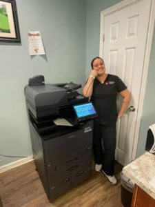 Smiling woman with copier in office—STAT Business Systems offers Kyocera copier leasing in Fort Lauderdale, South Florida.