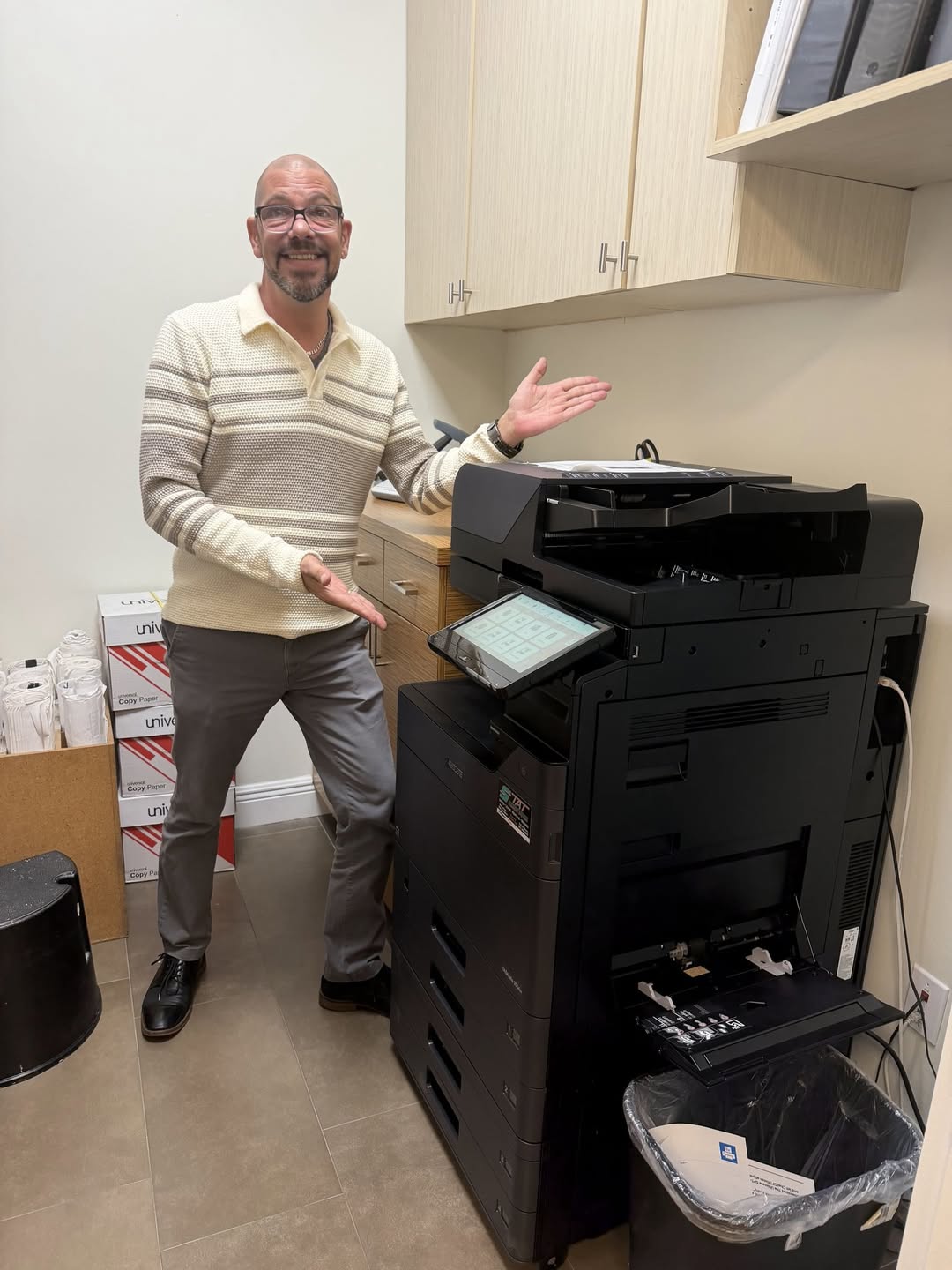Smiling property management professional posing next to a newly installed black Kyocera TASKalfa multifunction copier provided by STAT Business Systems.