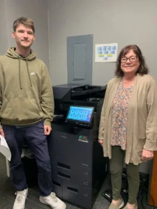 bdecfda1-1f58-49d2-8299-a931cf964d9dwebp - STAT Business Systems Two people stand beside a large multifunction printer in an office setting.