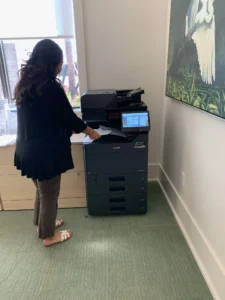 STAT article image Copier Page Allowances and Overages Read the Numbers - STAT Business Systems - STAT Business Systems Office employee using a multifunction copier beside a window